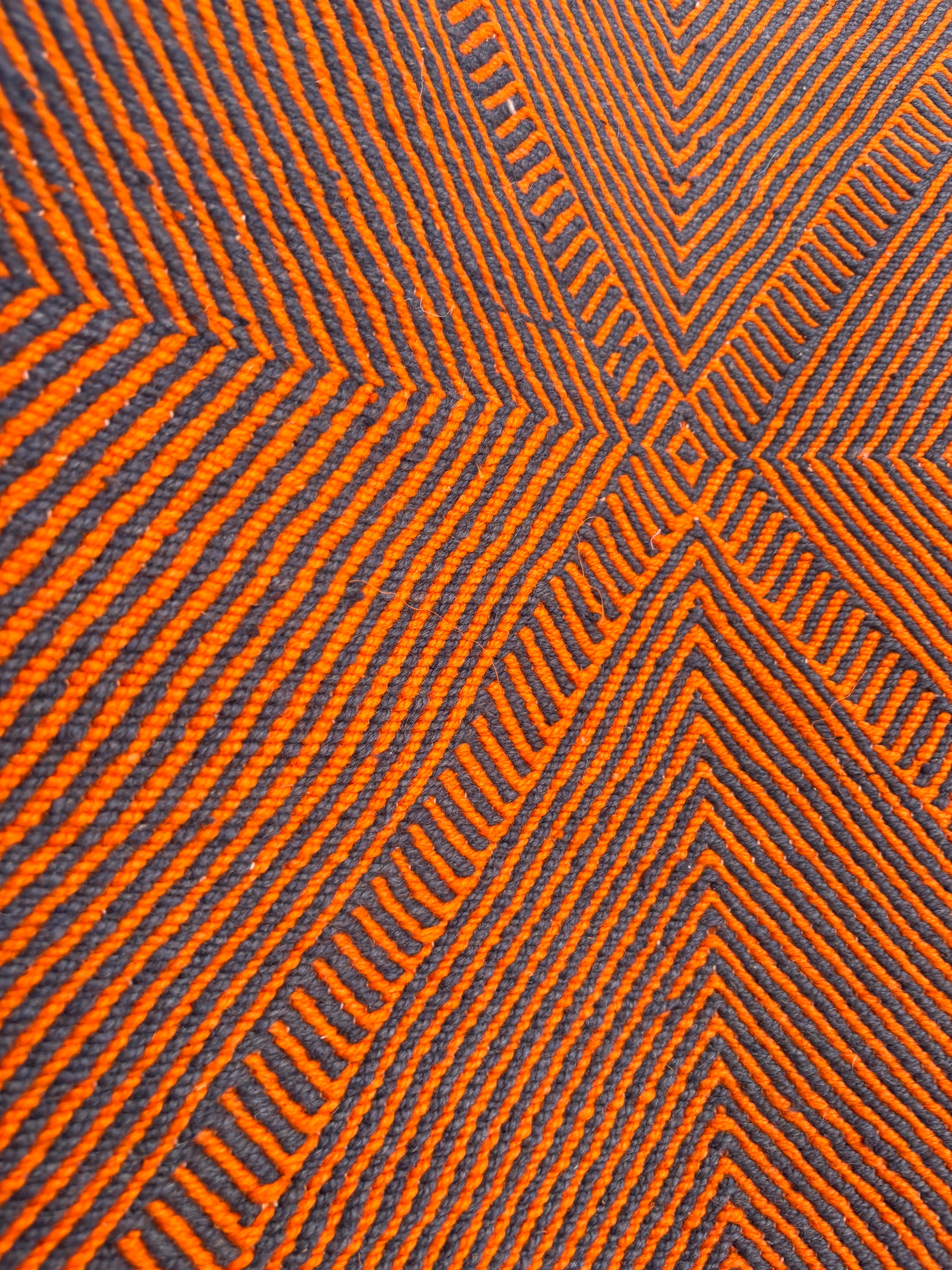 Die Nahaufnahme des LEY Teppichs "Rabina" 2,00 x 3,00 von LEY! zeigt orangefarbene und dunkelbraune Linien in geometrischen Mustern aus Rauten und Dreiecken, die eine optische Täuschung mit gleichmäßig verteilten, strukturierten Details erzeugen.