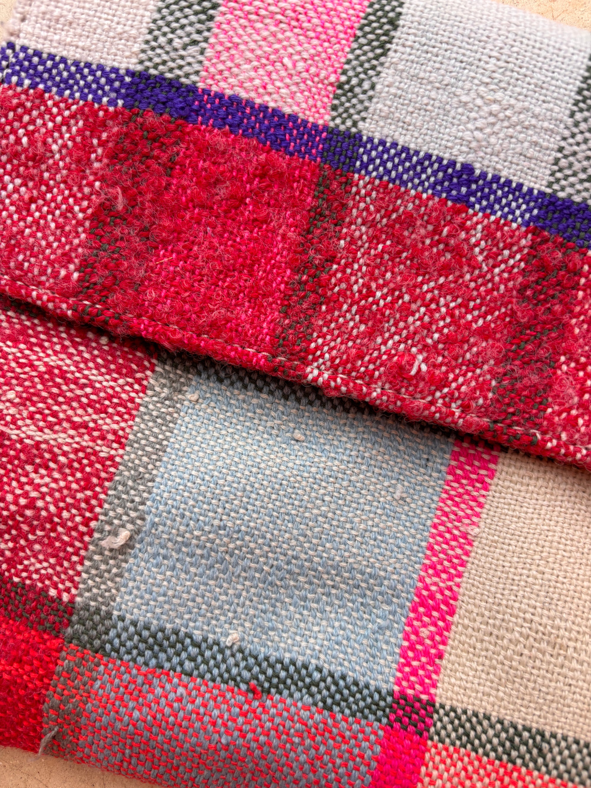 Nahaufnahme der Vintage Clutch von LEY! aus handgefertigten Wollstoffen mit karierten Mustern in Rot-, Rosa-, Lila-, Grau- und Blautönen, die die strukturierten Fäden und die leicht raue Oberfläche hervorheben.