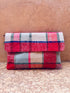 Die LEY! Vintage Clutch mit rot-weiß-grün-blauem Karomuster aus Upcycling Wolle steht vor einer rissigen, strukturierten beigen Wand auf dem Boden.