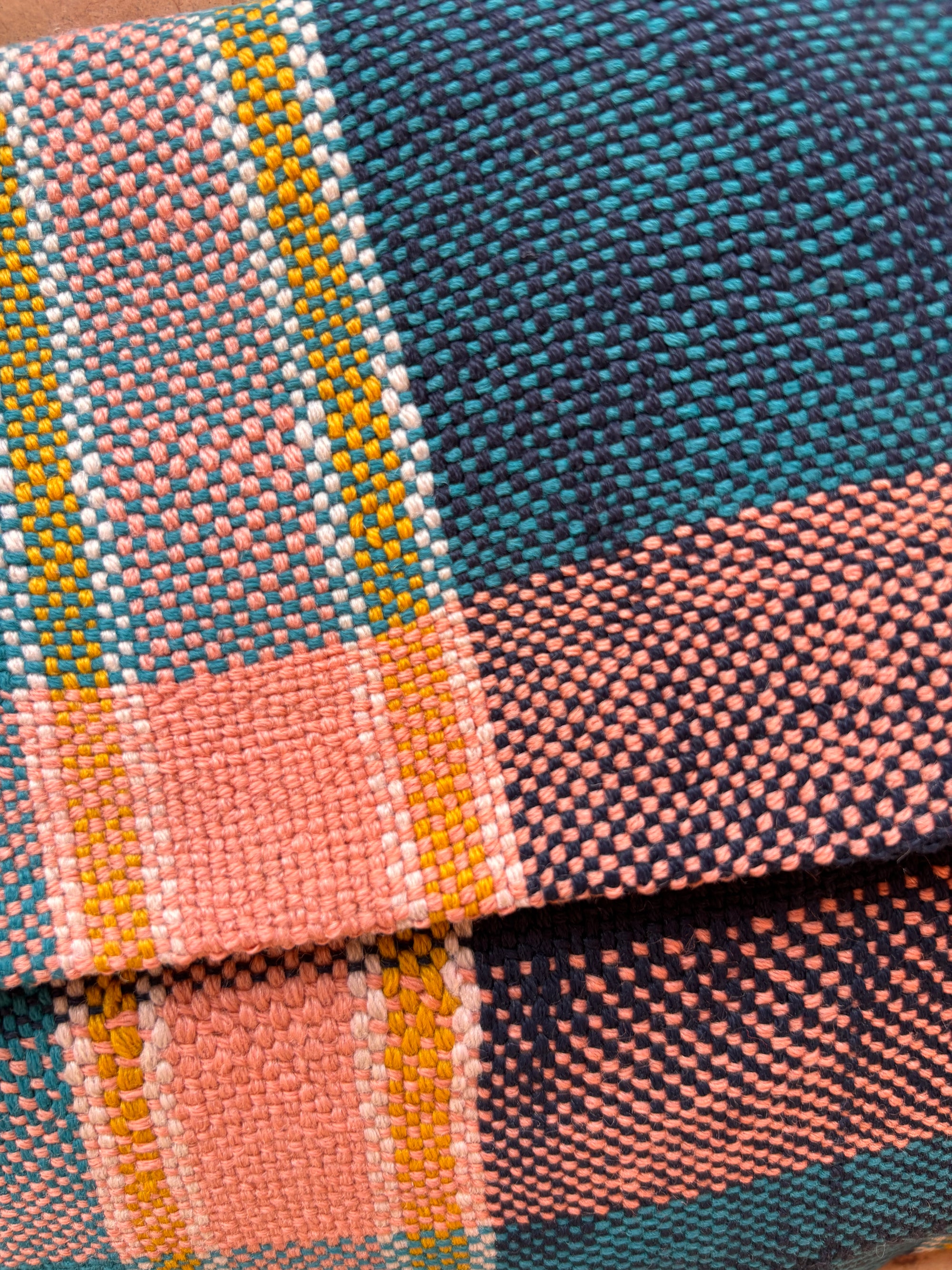 Nahaufnahme eines lebhaft karierten Wollstoffs in Pink, Teal, Gelb, Weiß und Marineblau. Die detaillierten Fäden spiegeln den Charme der handgefertigten Vintage Clutch von LEY! wider.