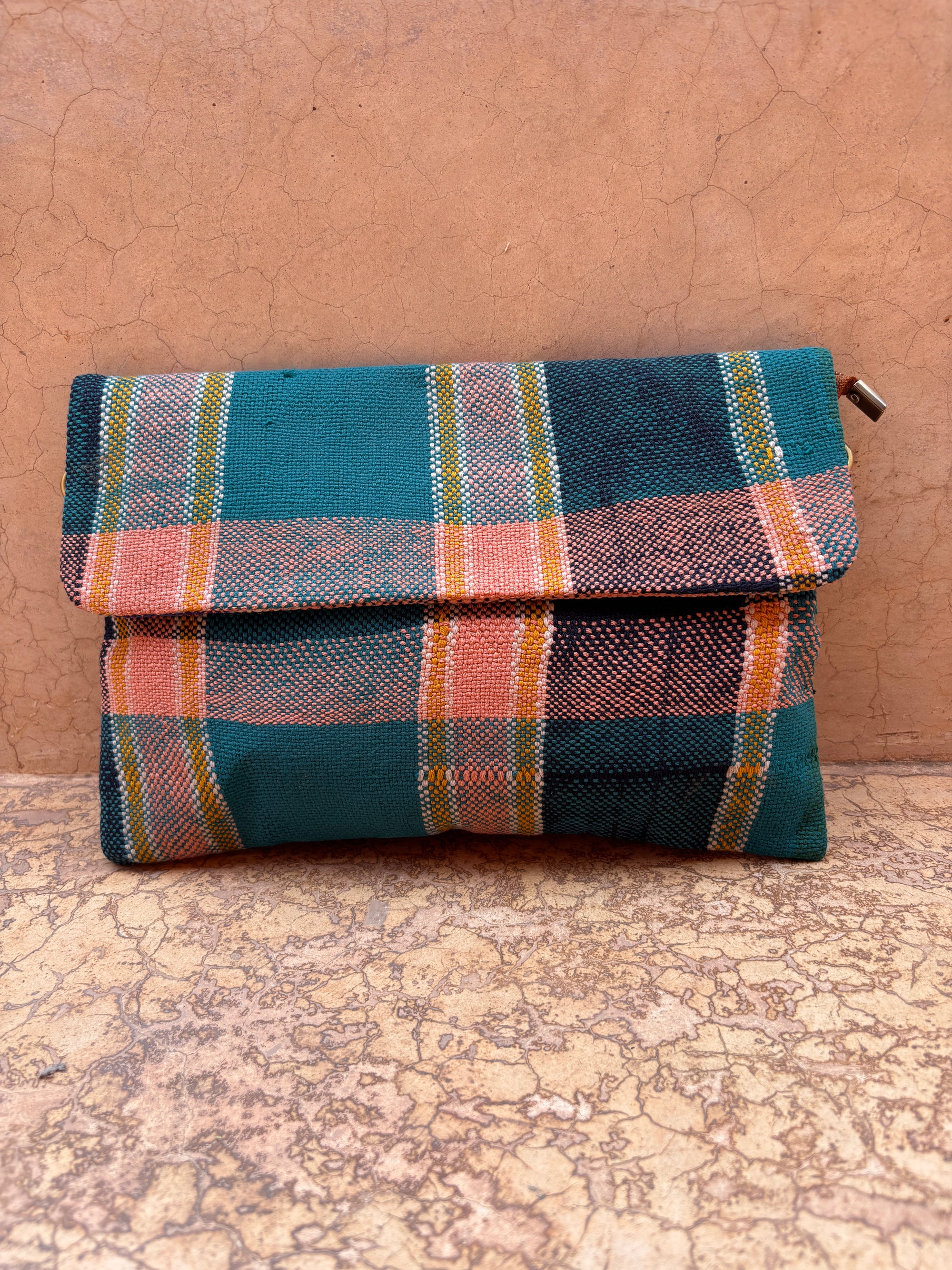 Die LEY! Vintage Clutch ist eine kleine, handgefertigte Tasche mit Überschlag, die ein grünes, orangefarbenes und rosafarbenes Karomuster auf einem braunen, strukturierten Hintergrund zeigt.