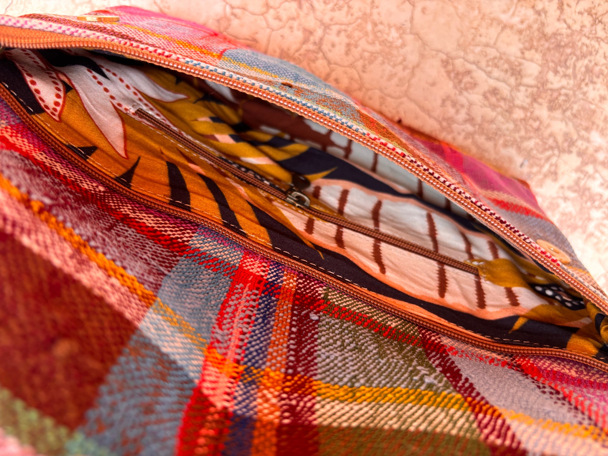 Eine Nahaufnahme der LEY! Vintage Clutch zeigt ihr offenes Karomuster und den roten Reißverschluss, der den Blick auf ein bunt gemustertes Futter freigibt. Die handgefertigte Tasche ist mit einer strukturierten, hellen Oberfläche versehen.