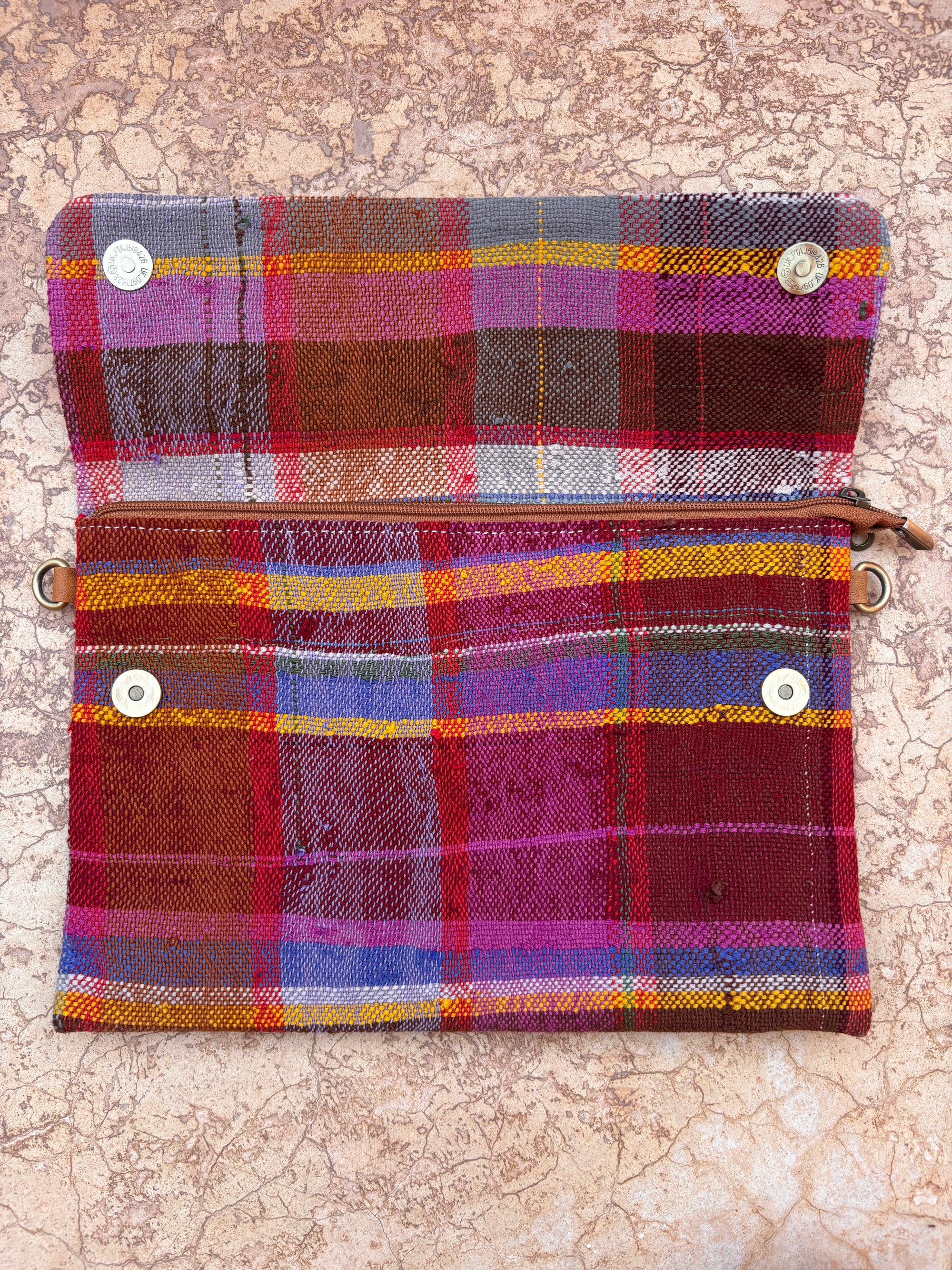 Die Vintage Clutch von LEY! ist eine lebhaft karierte Stofftasche aus klassischer Wolle mit rot, lila, gelb, grau und blau karierten Streifen. Sie liegt offen auf einer strukturierten beigen Oberfläche.