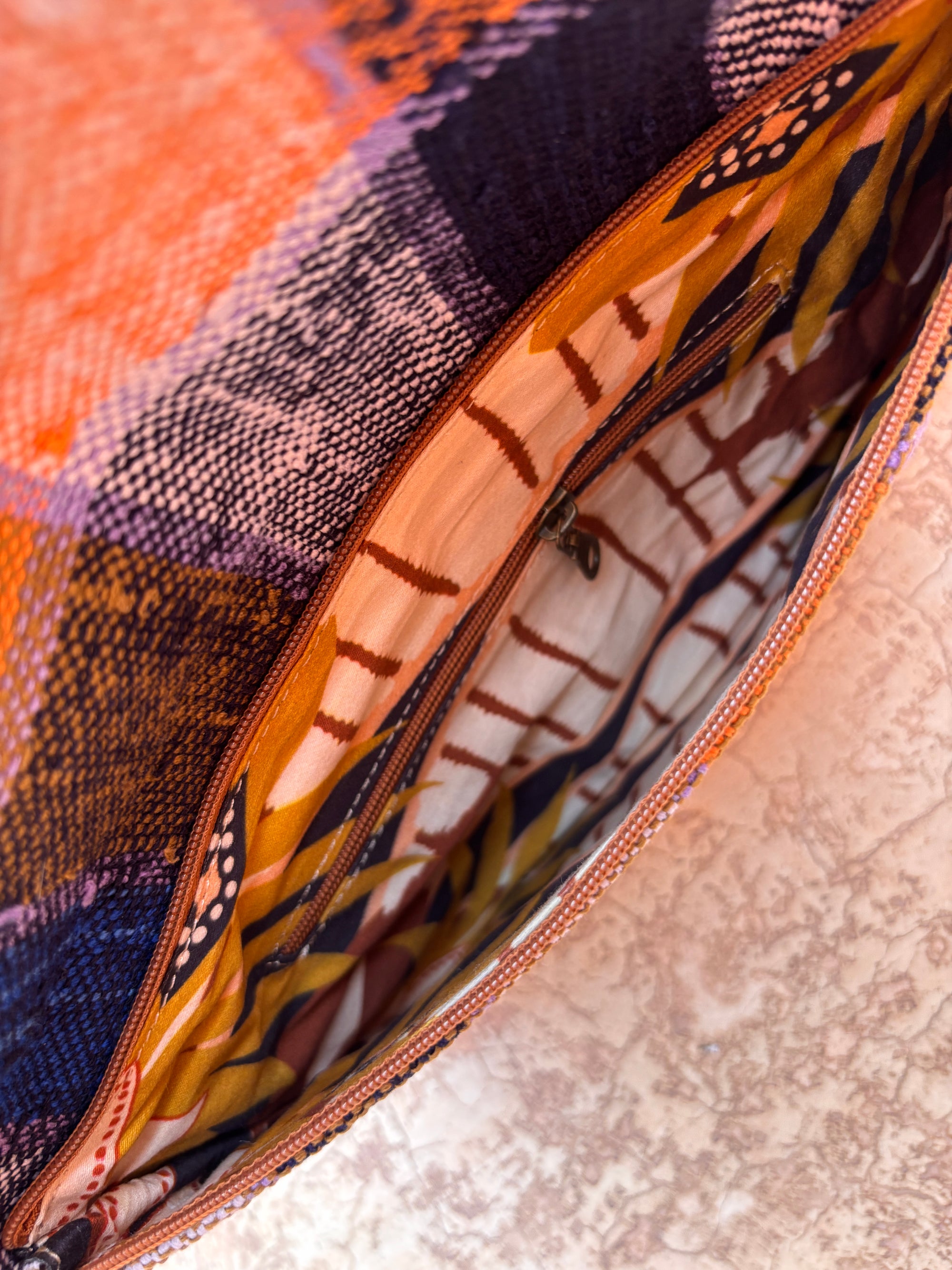 Nahaufnahme einer LEY! Vintage Clutch mit orange- und lilafarbenem Wollkaro auf der Außenseite und einem lebhaft gemusterten Stofffutter auf einer strukturierten, hellen Oberfläche.