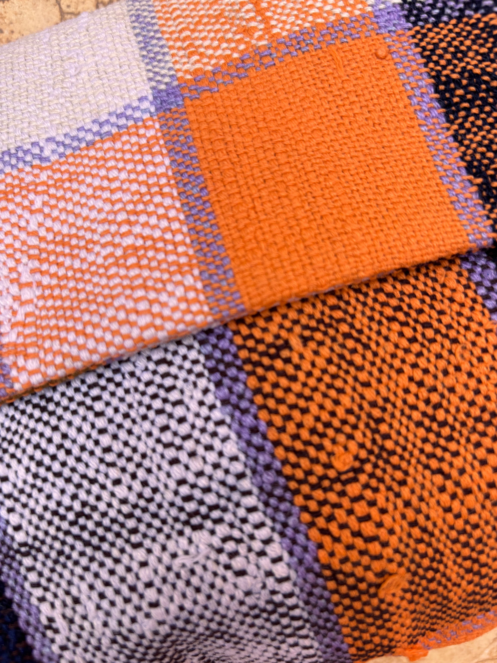 Nahaufnahme der LEY! Vintage Clutch mit einem handgewebten Stoff mit Karomuster in Orange, Lila, Schwarz und Weiß. Die detaillierte Textur und die sich überschneidenden Farben der Fäden sind deutlich sichtbar.