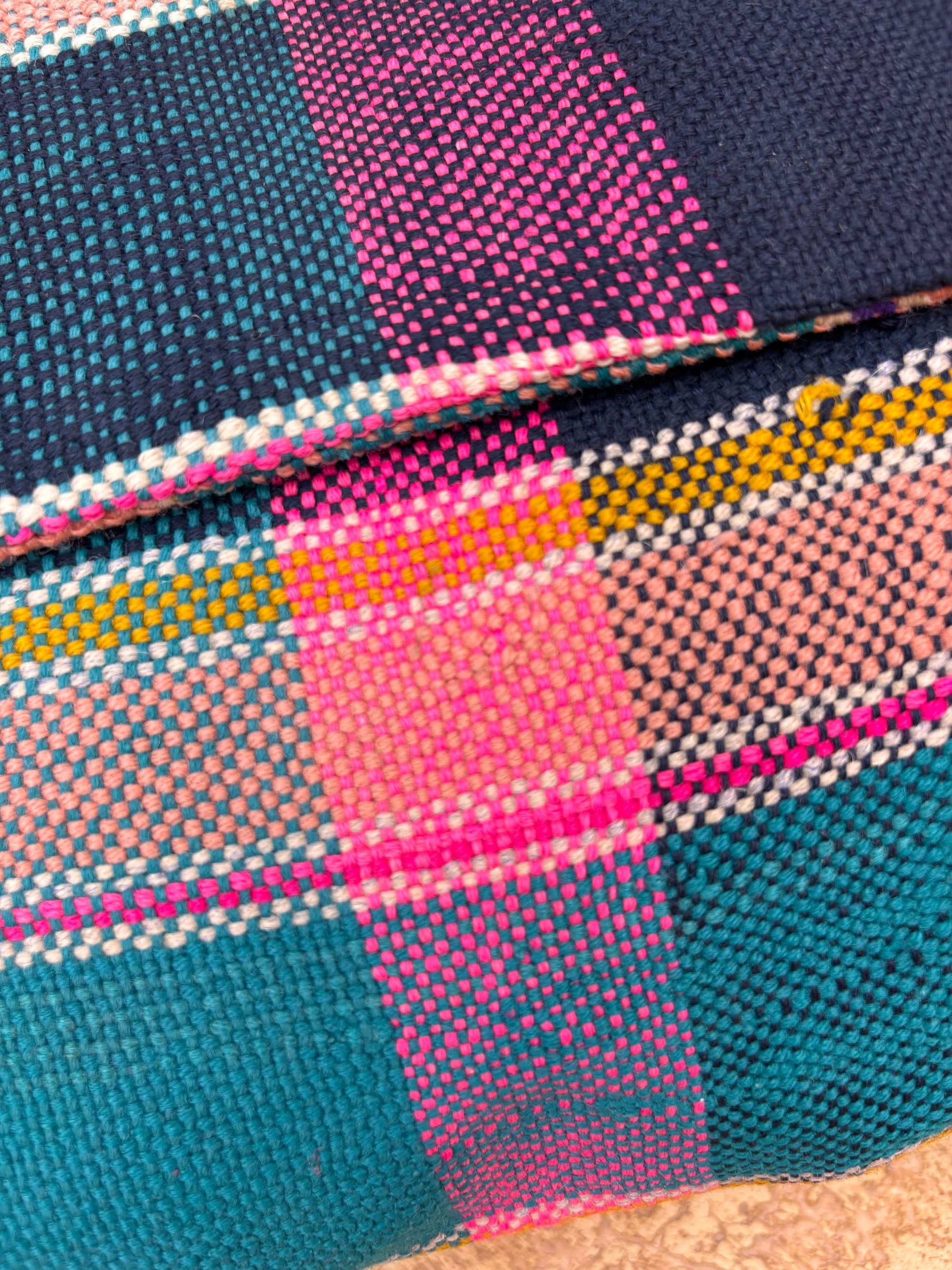 Nahaufnahme eines gewebten Stoffes mit marineblauem, blaugrünem, rosa, gelbem und pfirsichfarbenem Karomuster, das die sichtbare Fadentextur zeigt - perfekt für die LEY! Vintage Clutch, hergestellt aus feiner Wolle.