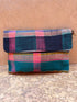 Die Vintage Clutch von LEY! zeigt ein leuchtendes Karomuster in Pink, Blau und Petrol und ruht auf einer strukturierten Steinoberfläche mit passendem Hintergrund - ein herausragendes Accessoire für jede Sammlung.
