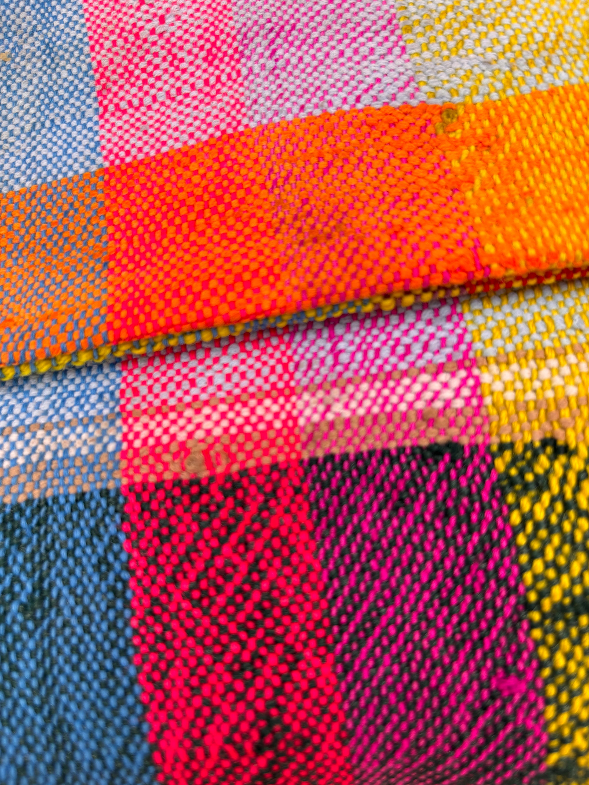 Eine Nahaufnahme der LEY! Vintage Clutch zeigt ihr farbenfrohes Karomuster in leuchtendem Pink, Gelb, Orange, Blau und Weiß mit deutlich sichtbarer handgewebter upgecycelter Wolltextur und Fäden.
