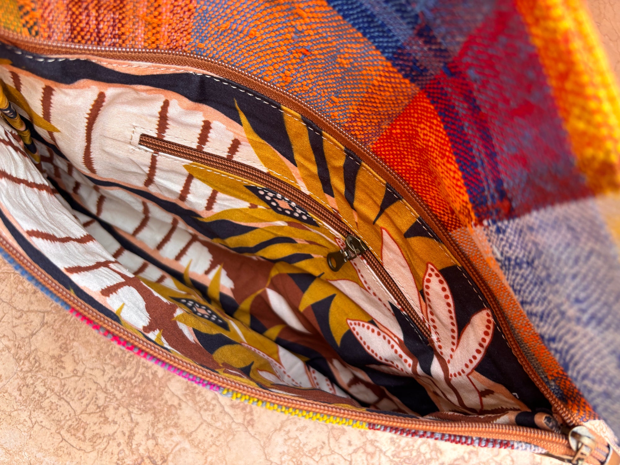 Nahaufnahme der LEY! Vintage Clutch, handgefertigt aus upgecycelter Wolle mit einer bunt karierten Außenseite und einer gemusterten Innenseite aus braunem, gelbem und weißem Stoff mit Blättern, abstrakten Motiven und einer Innentasche mit Reißverschluss.