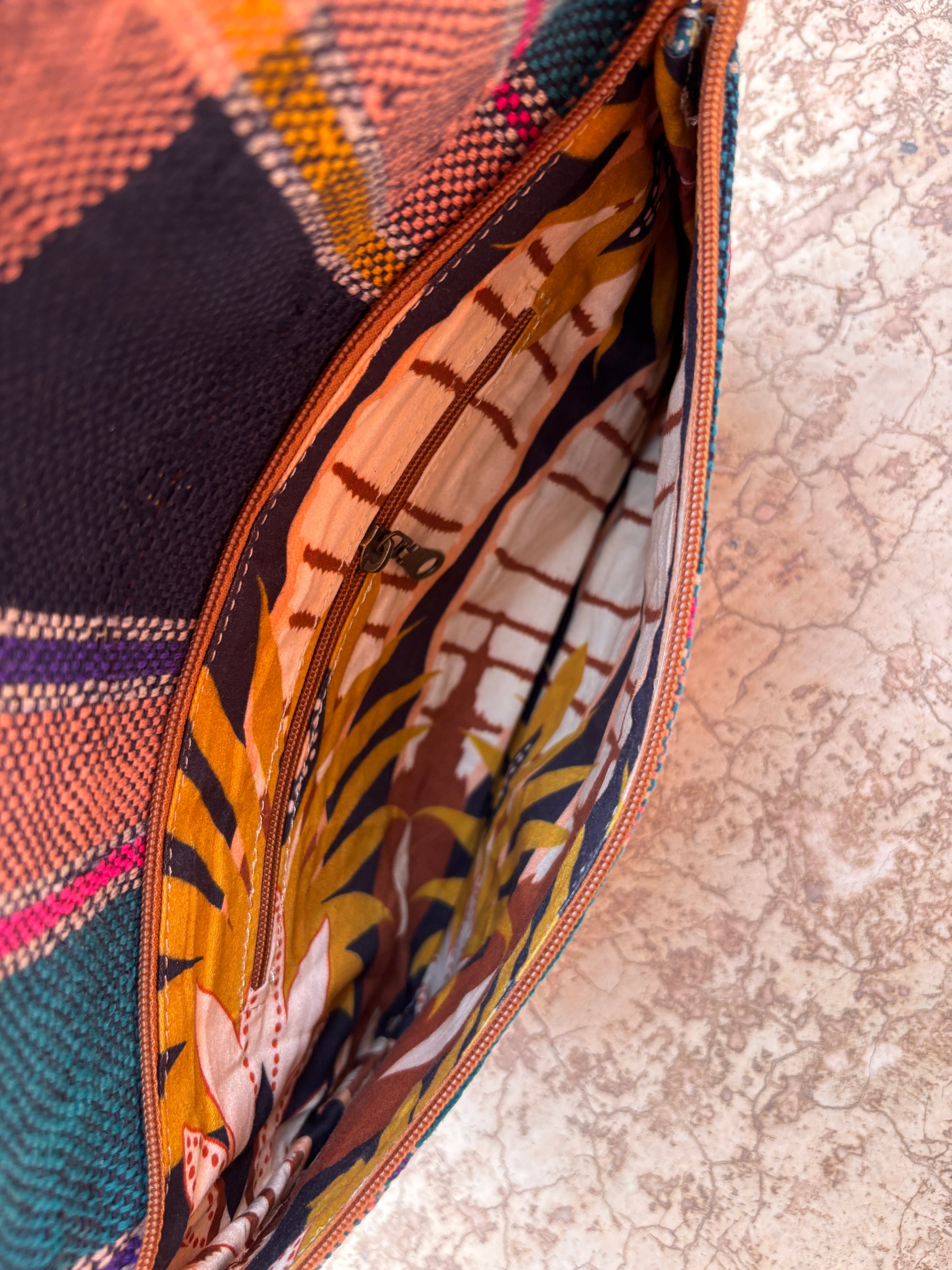 Eine Nahaufnahme der Vintage Clutch von LEY! - eine bunte, handgewebte Tasche mit gemustertem Stofffutter und einer Innentasche mit Reißverschluss - liegt auf einer strukturierten Oberfläche.