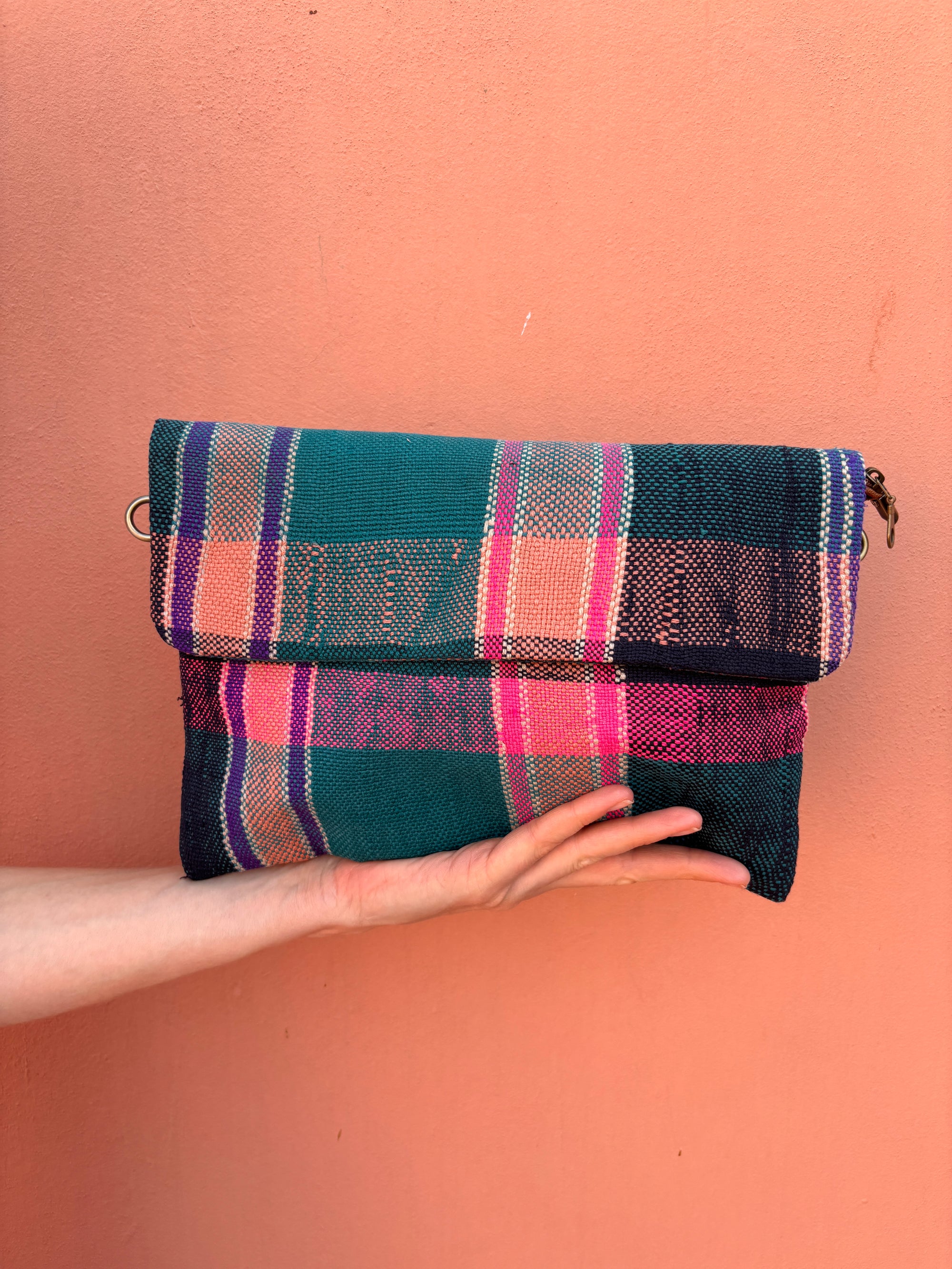 Eine Hand zeigt die LEY! Vintage Clutch, die aus handgewebter Wolle in leuchtendem Teal, Pink und Lila vor einer pfirsichfarbenen Wand gefertigt wurde.