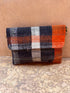 Die LEY! Vintage Clutch, eine kleine rechteckige Tasche mit Überschlag und auffälligem Karomuster in Marineblau, Orange, Weiß und Schwarz, wird vor einer beigefarbenen Wand und einem beigen Boden präsentiert.