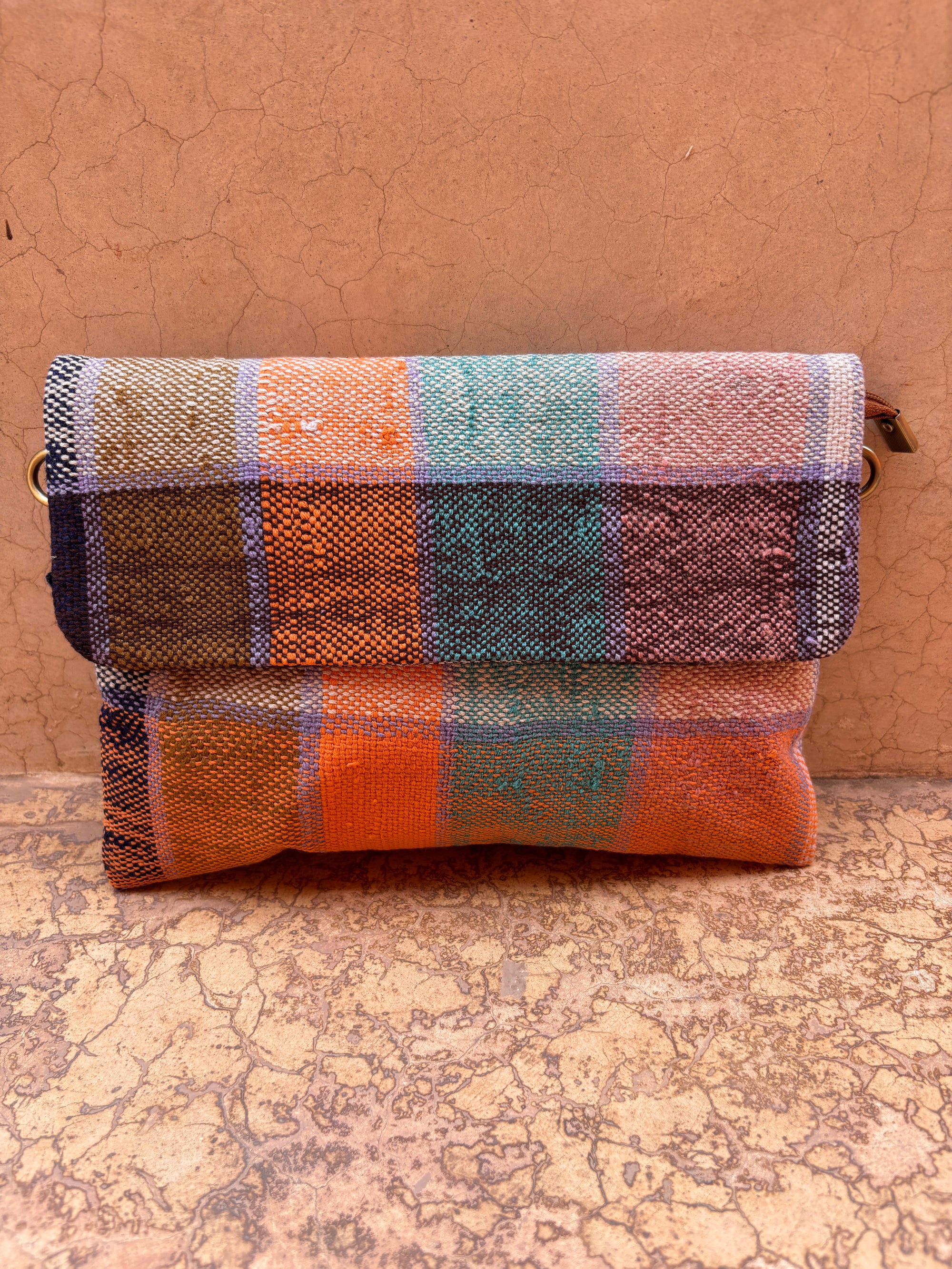 Die LEY! Vintage Clutch zeichnet sich durch ein handgewebtes Karomuster in Orange, Blau, Lila und Beige aus - perfekt für ein einzigartiges Accessoire. Die leuchtenden Farben und die hochwertige Verarbeitung heben sich von jedem Hintergrund ab.