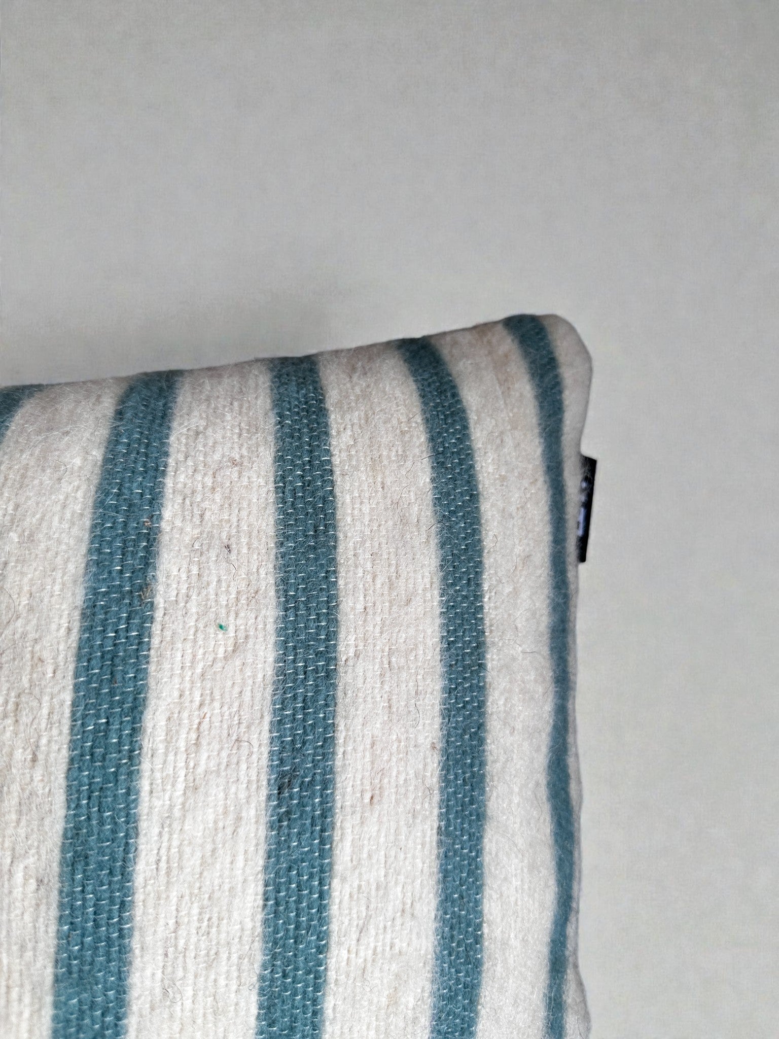 Eine Nahaufnahme des LEY! Kissen - WINTER EDITION - Lagune - 30x50, mit vertikalen Streifen in Teal und Weiß, wobei nur die Ecke dieses weichen Kissens vor einem schlichten, hellen Hintergrund zu sehen ist.