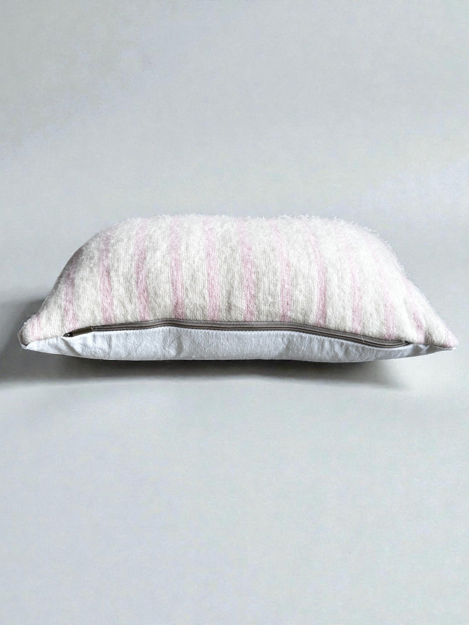 Das Kissen - WINTER EDITION - Puder- 30 x 50 von LEY! ist ein rechteckiges Kissen aus Schurwolle mit einem weichen, strukturierten Bezug mit vertikalen Streifen in Rosa und Weiß auf einem hellgrauen Hintergrund - ideal, um Ihrem Raum einen gemütlichen Stil zu verleihen.