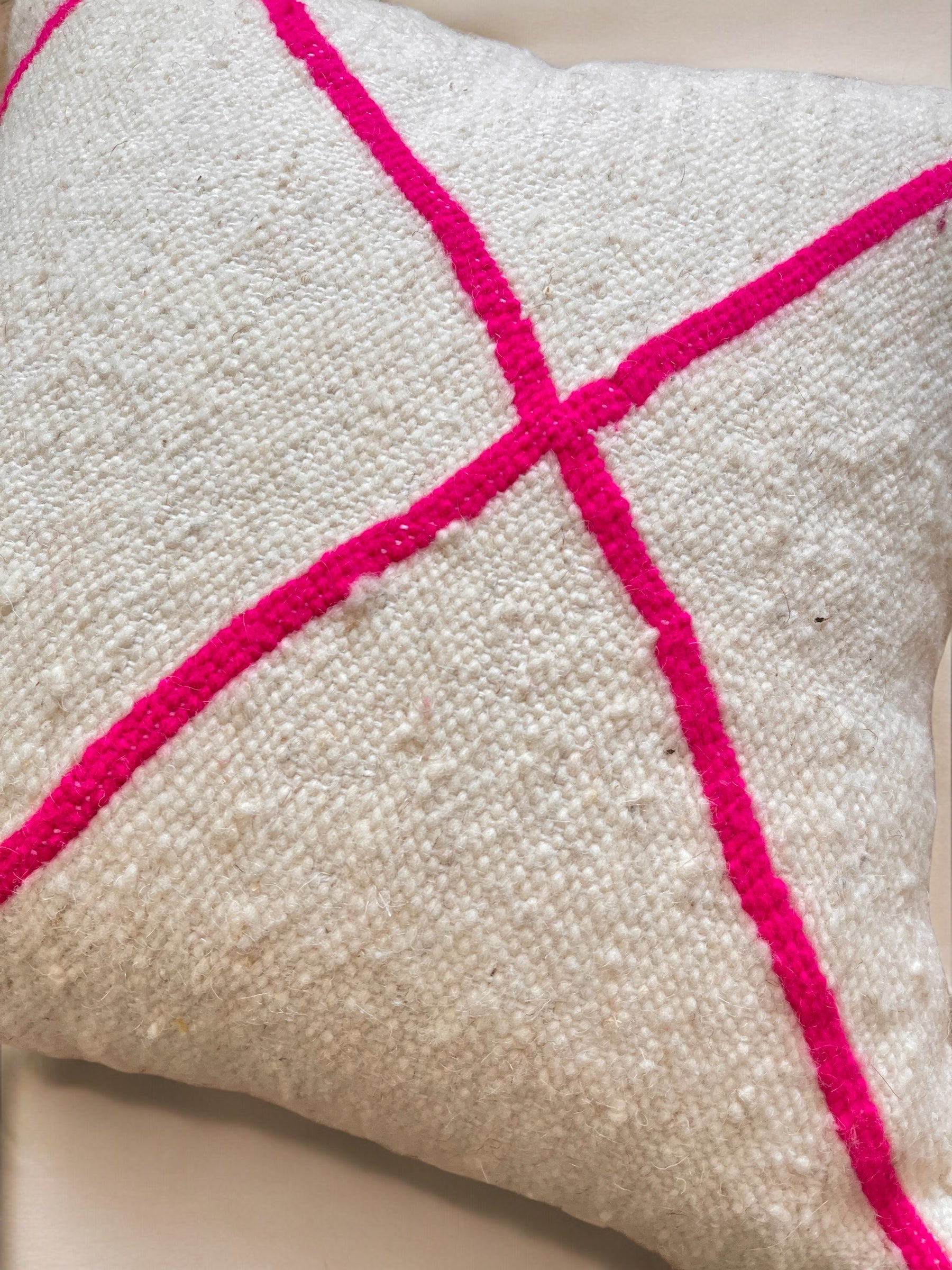 Das Kissen - Mina 50x50 von LEY! ist ein weißes, strukturiertes Kissen mit zwei leuchtend rosafarbenen Linien in einem "X"-Muster - perfekt, um Ihrem Raum einen handgefertigten Marrakesch-Touch zu verleihen.
