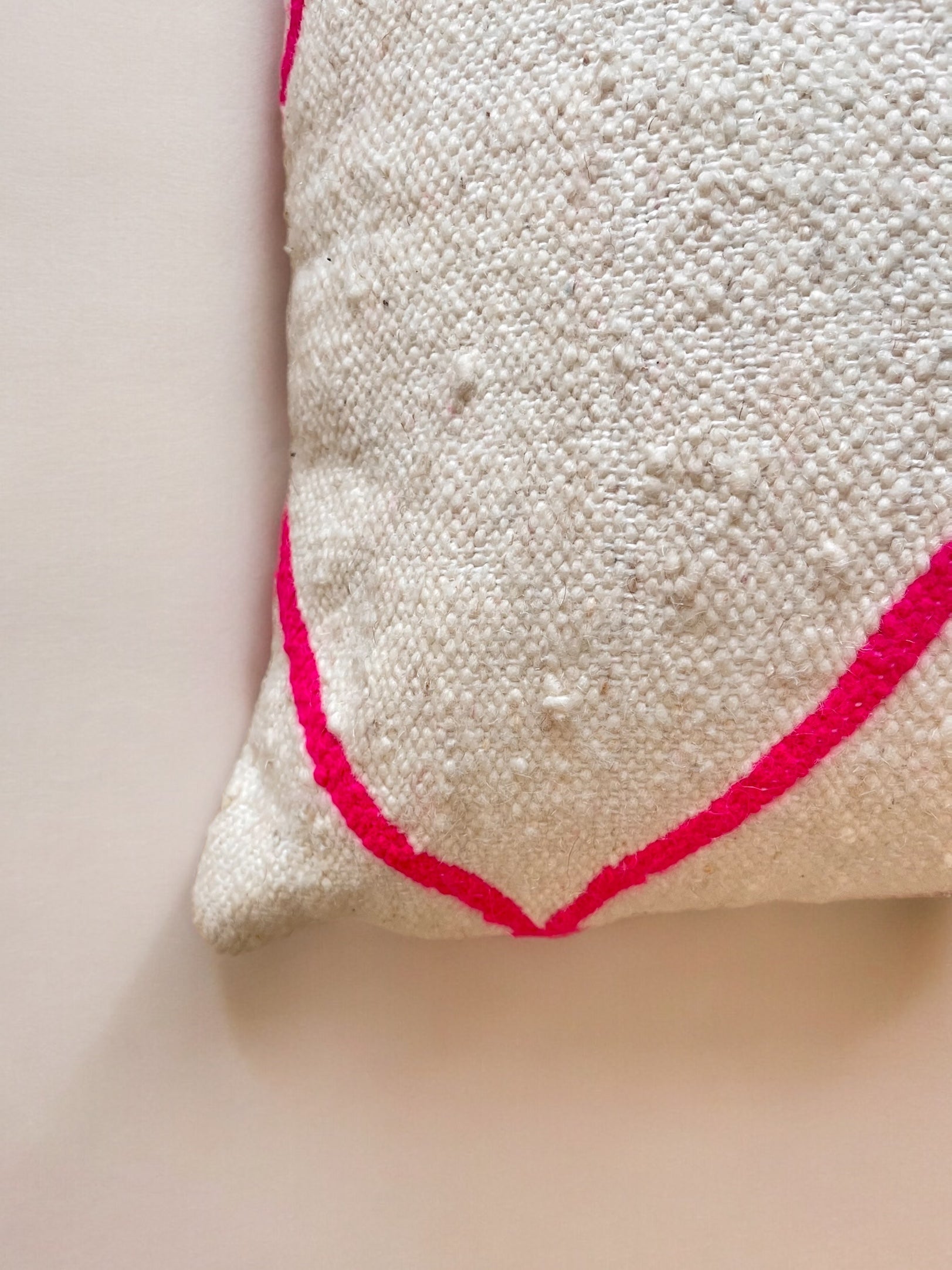 Nahaufnahme der Ecke des Kissens - Mina 50x50 von LEY! mit einem leuchtend rosa Diagonalstreifen auf strukturiertem weißem Stoff, handgefertigt in Marrakesch und auf einer hellen Oberfläche abgebildet.