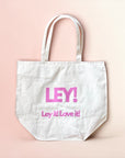 Die LEY! BAGS aus weißem Segeltuch trägt den Schriftzug "LEY!" in fetten rosa Buchstaben und darunter "Ley it! Love it!" auf einem hellrosa-beigen Hintergrund - perfekt für Fans von nachhaltigen Tragetaschen mit Markenzeichen.