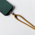 Eine dunkelgrüne Handyhülle mit dem Schlüsselanhänger Gold von LEY!, einem eleganten Handy-Accessoire, wird an ihrer Ecke befestigt und auf eine weiße Fläche gestellt.