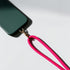 Der LEY! Schlüsselanhänger Pink, ein leuchtend pinkes, geflochtenes Schlüsselband, ist mit einer Metallschließe an einer grünen Smartphone-Hülle befestigt und ruht auf einer weißen Oberfläche mit weichen Schatten.