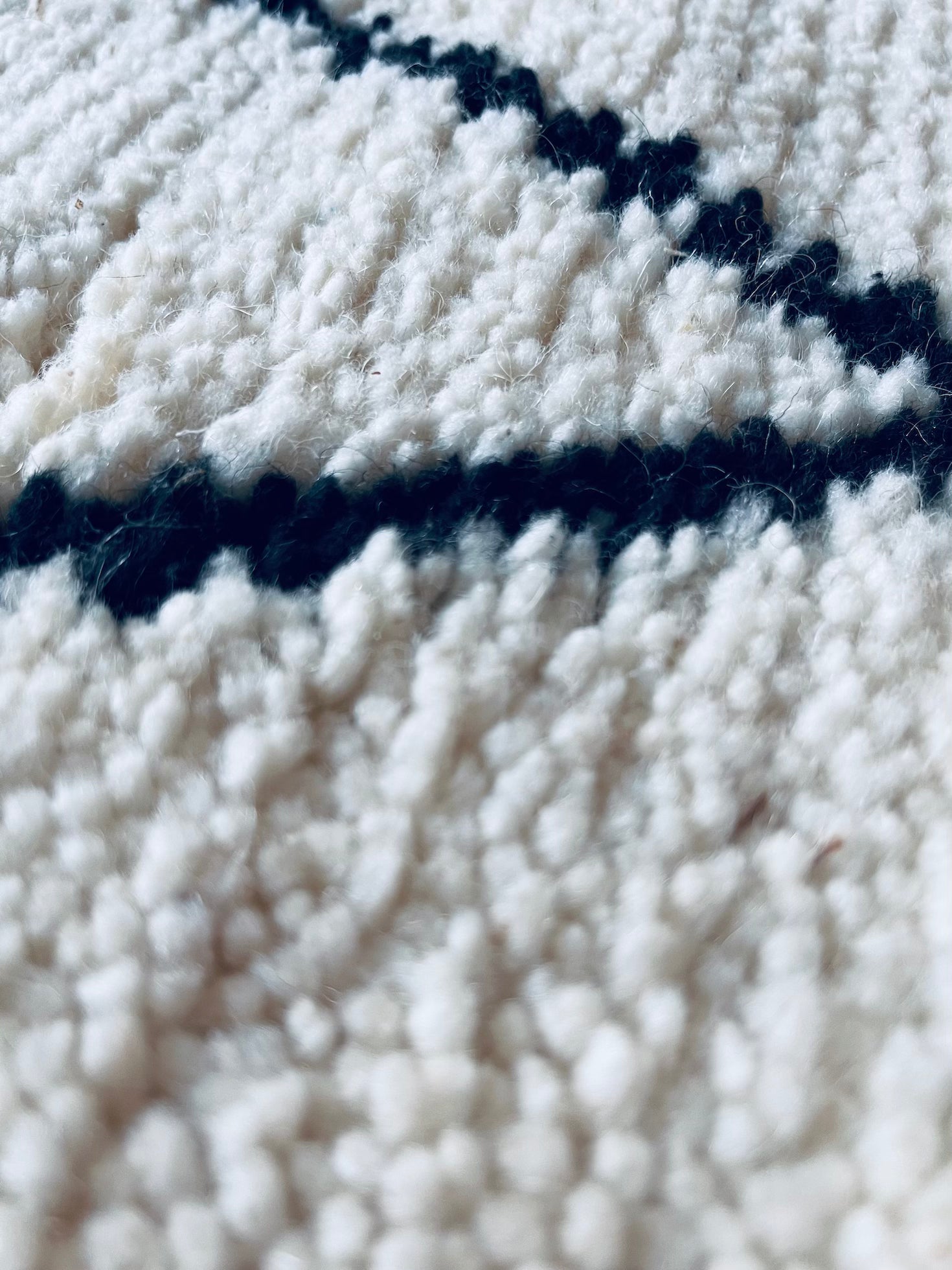 Nahaufnahme von THE DANISH GIRL INTERIOR BERBER TEPPICH - MAHIMA (1,50 x 2,50m), handgeknüpft aus natürlicher Wolle in Weiß mit schwarzen linearen Mustern. Oberflächendetails und Fasern sorgen für einen weichen, taktilen Look.
